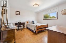 Spacious bedroom showcasing warm hardwood flooring and an abundance of natural light from a large window. - 