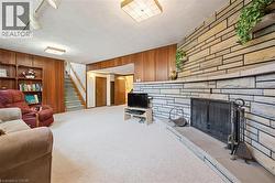 Stone-clad fireplace with a hearth and metal grate, wood paneling, built-in shelving, white carpeting, and a staircase with wood railing - 
