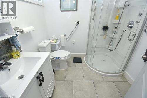 Modern bathroom featuring a clean-lined vanity with integrated sink, ceramic tile flooring, and a corner walk-in shower enclosure with multiple showerheads and grab bars - 10 Craddock Boulevard, Jarvis, ON - Indoor Photo Showing Bathroom