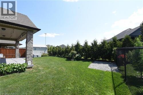 Expansive backyard featuring a covered patio with stone-clad columns, a manicured lawn, a gravel-covered area, and mature evergreen privacy hedging - 10 Craddock Boulevard, Jarvis, ON - Outdoor With Deck Patio Veranda