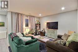 Comfortable living room featuring dual seating arrangements with a green upholstered sofa and brown sectional, recessed ceiling lighting, wall-mounted flat-screen television on a light-finish media co - 