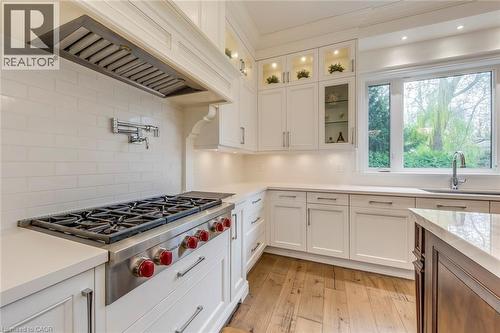 Gourmet kitchen featuring a professional-grade gas range, pot filler, recessed lighting, white cabinetry with display uppers, and wood-finish flooring - 436 Willis Drive, Oakville, ON - Indoor Photo Showing Kitchen With Upgraded Kitchen