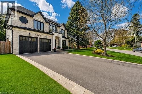 Stately stone and siding exterior featuring a prominent arched entryway, black-framed windows, and two large black garage doors - 436 Willis Drive, Oakville, ON - Outdoor