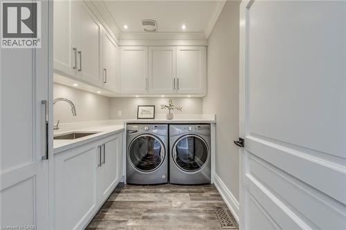 Laundry area featuring white shaker-style cabinetry with chrome hardware, an undermount sink with a gooseneck faucet, light-toned countertops, and wood-finish flooring - 436 Willis Drive, Oakville, ON - Indoor Photo Showing Laundry Room