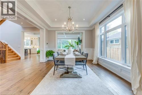 Dining area featuring wood-finish flooring, a coffered ceiling with recessed lighting, an ornate chandelier, large picture windows with white trim, and wainscoting - 436 Willis Drive, Oakville, ON - Indoor Photo Showing Dining Room