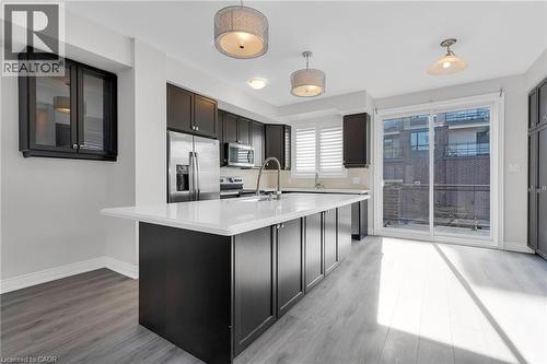 Modern kitchen featuring a large central island with a white countertop, dark flat-panel cabinetry, stainless steel appliances, and light wood-finish flooring - 2 Waterview Lane, Grimsby, ON - Indoor Photo Showing Kitchen With Upgraded Kitchen