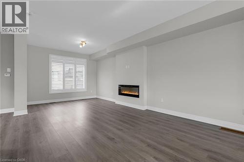 Spacious living area featuring wide-plank wood-finish flooring, a contemporary linear electric fireplace, and a large window with white plantation shutters - 2 Waterview Lane, Grimsby, ON - Indoor Photo Showing Living Room With Fireplace