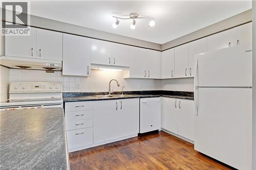 Kitchen featuring white cabinetry, dark speckled countertops, a white tile backsplash, wood-finish flooring, and a white appliance suite - 129 Kovac Road, Cambridge, ON - Indoor Photo Showing Kitchen