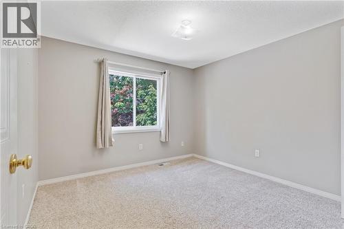 Carpeted room featuring a white-framed window, neutral gray wall tones, white baseboards, and a ceiling-mounted light fixture - 129 Kovac Road, Cambridge, ON - Indoor Photo Showing Other Room