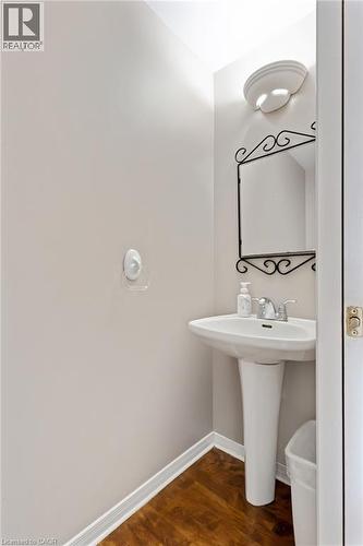 Pedestal sink with chrome faucet, complemented by wood-finish flooring and white baseboards - 129 Kovac Road, Cambridge, ON - Indoor Photo Showing Bathroom