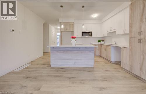 Modern kitchen featuring a spacious open floor plan with a substantial waterfall-edge island, white cabinetry, wood-finish flooring throughout, stainless steel appliances including a built-in microwav - 89 Rivergreen Crescent, Cambridge, ON - Indoor Photo Showing Kitchen