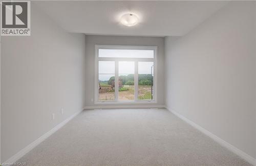 Bright interior space featuring a large multi-pane window, neutral-toned walls, plush carpeting, white baseboards, and a ceiling-mounted light fixture - 89 Rivergreen Crescent, Cambridge, ON - Indoor Photo Showing Other Room