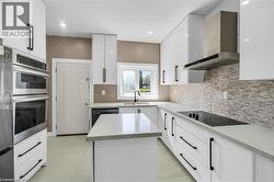 Contemporary kitchen featuring white cabinetry with matte black hardware, light-toned countertops, a multi-tone tile backsplash, and stainless steel appliances - 