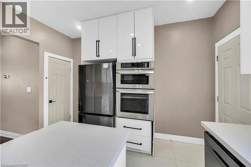 Modern kitchen featuring white cabinetry with black hardware, stainless steel French-door refrigerator, and dual wall-mounted convection ovens with microwave - 334 Cannon Street E, Hamilton, ON - Indoor Photo Showing Kitchen