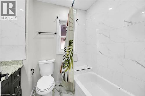 Bathroom featuring a built-in tub with marble-look tile surround, a dark wood vanity with a speckled countertop, and a window - 334 Cannon Street E, Hamilton, ON - Indoor Photo Showing Bathroom