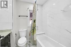 Bathroom featuring a built-in tub with marble-look tile surround, a dark wood vanity with a speckled countertop, and a window - 