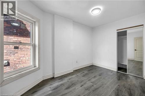 Spacious bedroom with wood-finish flooring, abundant natural light from large window with brick exterior views, mirrored closet doors, and recessed ceiling lighting - 334 Cannon Street E, Hamilton, ON - Indoor Photo Showing Other Room