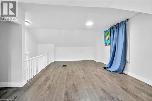 Spacious upper-level room featuring wood-finish flooring, a white spindle railing, and a window with blue drapes - 334 Cannon Street E, Hamilton, ON - Indoor