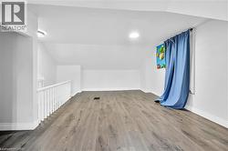 Spacious upper-level room featuring wood-finish flooring, a white spindle railing, and a window with blue drapes - 