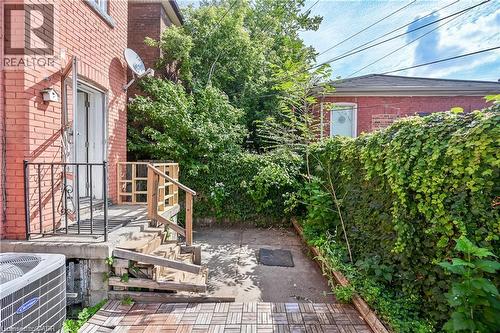 Rear exterior featuring a brick facade, ground-level patio, and a privacy hedge - 334 Cannon Street E, Hamilton, ON - Outdoor