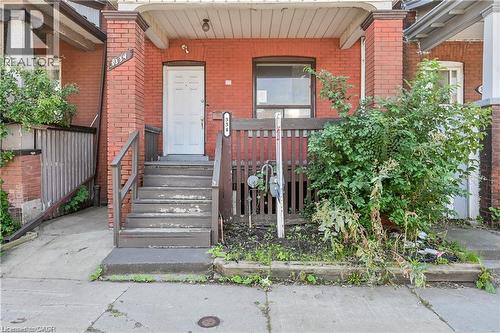 Brick facade residence featuring a white paneled entry door, front porch with wood railings and steps, and a concrete walkway - 334 Cannon Street E, Hamilton, ON - Outdoor