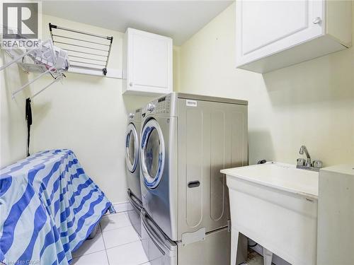 Dedicated laundry area featuring a utility sink, white wall-mounted cabinetry, and tiled flooring - 584 Pinery Trail, Waterloo, ON - Indoor Photo Showing Laundry Room