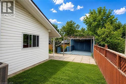 Rear exterior featuring white horizontal siding, a covered patio area with a blue floor, a metal frame structure, a wood privacy fence, and a manicured lawn - 182 Avalon Place, Kitchener, ON - Outdoor With Exterior