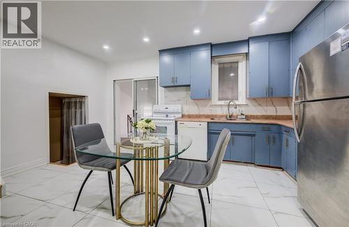 Functional kitchen space featuring blue cabinetry, white appliances, a stainless steel refrigerator, and a white tile floor - 182 Avalon Place, Kitchener, ON - Indoor