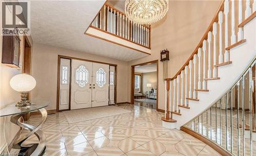 Grand foyer featuring double entry doors with decorative glass, a curved staircase with wood treads and white balusters, an upper-level balcony, and a multi-tiered chandelier - 28 Walnut Drive, Guelph, ON - Indoor Photo Showing Other Room