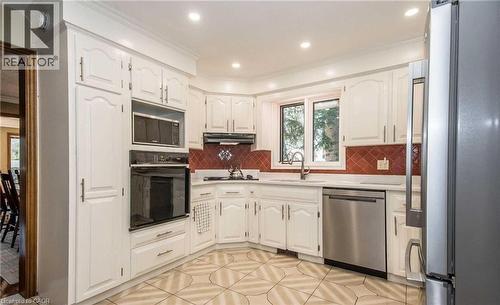 White cabinetry with crown molding, stainless steel built-in appliances, red tile backsplash, white countertops, and patterned tile flooring - 28 Walnut Drive, Guelph, ON - Indoor Photo Showing Kitchen
