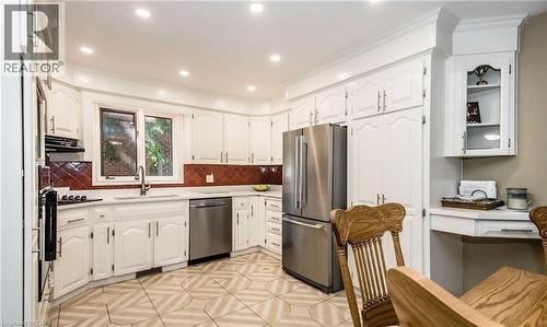 White cabinetry with crown molding, stainless steel appliances, a tile backsplash, recessed lighting, and a built-in desk area - 28 Walnut Drive, Guelph, ON - Indoor Photo Showing Kitchen