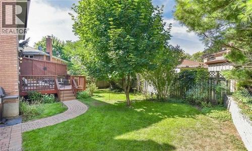 Expansive backyard oasis featuring a mature tree canopy, lush manicured lawn, and curved brick hardscape pathway - 28 Walnut Drive, Guelph, ON - Outdoor With Deck Patio Veranda