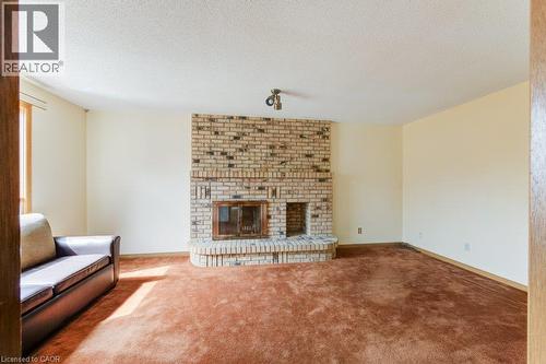 Spacious room featuring a prominent brick fireplace with a raised hearth and integrated wood storage - 27 Walmer Gardens, London, ON - Indoor Photo Showing Living Room With Fireplace