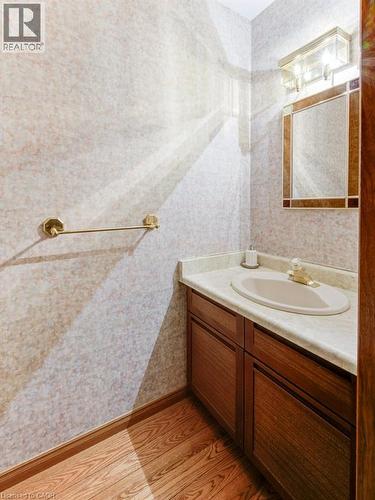 Vanity with an integrated sink and light-toned countertop, wood-finish flooring, and a wall-mounted light fixture - 27 Walmer Gardens, London, ON - Indoor Photo Showing Bathroom