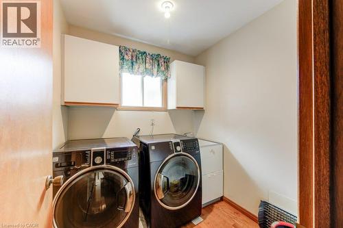 Dedicated laundry space featuring wood-finish flooring, a window providing natural light, and upper cabinetry for storage - 27 Walmer Gardens, London, ON - Indoor Photo Showing Laundry Room