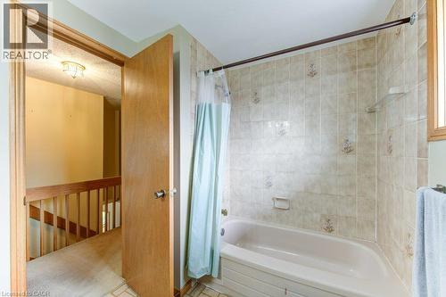 Bathroom featuring a bathtub with tiled surround, light-colored wall tiles with decorative accents, and an overhead bath rod - 27 Walmer Gardens, London, ON - Indoor Photo Showing Bathroom