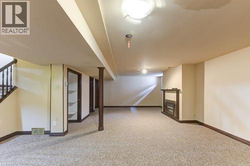 Carpeted lower-level room featuring a fireplace with a dark wood mantel, recessed lighting, and a dark wood staircase with a balustrade - 27 Walmer Gardens, London, ON - Indoor Photo Showing Other Room