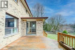 Exterior brick facade featuring a wood deck with wood railings, sliding glass door access, and an expansive grassy area - 