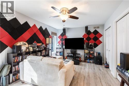 Spacious recreational room featuring wood-finish flooring, built-in shelving and media cabinetry, geometric accent wall with red and black diamond paneling, ceiling fan with integrated lighting, and a - 907 Doon Village Road, Kitchener, ON - Indoor Photo Showing Living Room