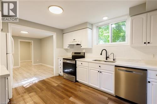 Renovated kitchen featuring white cabinetry, light-colored countertops, stainless steel appliances, a black matte faucet, and wood-finish flooring - 907 Doon Village Road, Kitchener, ON - Indoor Photo Showing Kitchen With Double Sink