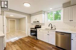 Renovated kitchen featuring white cabinetry, light-colored countertops, stainless steel appliances, a black matte faucet, and wood-finish flooring - 