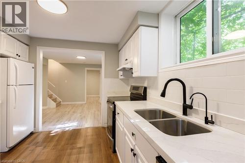 Contemporary kitchen featuring dual stainless steel undermount sinks with matte black gooseneck faucets, white shaker-style cabinetry, subway tile backsplash, and wood-finish flooring - 907 Doon Village Road, Kitchener, ON - Indoor Photo Showing Kitchen With Double Sink