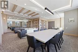 Spacious common area featuring recessed lighting, a coffered ceiling with wood-finish accents, extensive built-in shelving, and broad windows - 