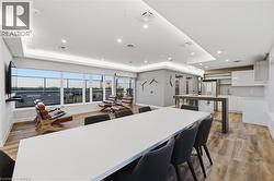 Open-concept common area featuring wood-finish flooring, a full bank of windows, recessed lighting, and a modern kitchen area with stainless steel appliances - 