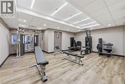Dedicated fitness center featuring modern exercise equipment, wood-finish flooring, recessed lighting, drop ceiling panels, and neutral wall tones - 
