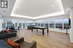 Spacious recreation room featuring a central billiard table, extensive window line, wood-finish flooring, and a drop ceiling with recessed lighting - 