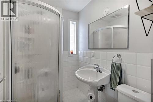 Compact bathroom featuring a curved shower enclosure with frosted glass, a pedestal sink with chrome faucet, a wall-mounted mirror, and white square tile wainscoting - 371 Ottawa Street S, Kitchener, ON - Indoor Photo Showing Bedroom