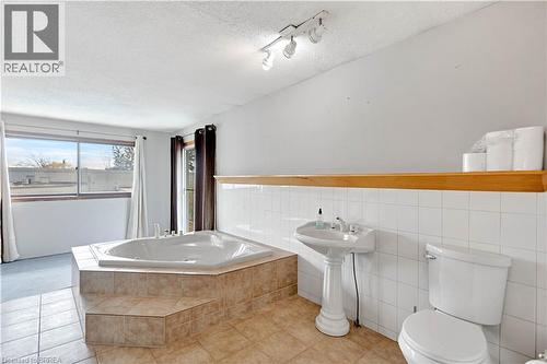 Spacious bathroom featuring an oversized corner soaking tub with tiled surround, pedestal sink, and tiled flooring - 371 Ottawa Street S, Kitchener, ON - Indoor Photo Showing Bedroom