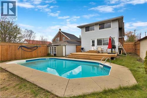 Backyard featuring a clear blue swimming pool with concrete surround, a multi-level wood deck, light-colored horizontal siding on the home's exterior, and a wood privacy fence - 371 Ottawa Street S, Kitchener, ON - Outdoor With In Ground Pool With Backyard