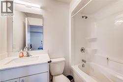 Bathroom featuring a vanity with a white countertop and integrated sink, a wall-mounted mirror, overhead lighting, a toilet, and a combined shower-bathtub unit - 